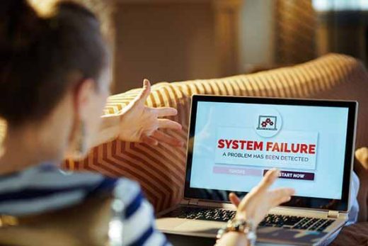 A shocked lady throwing her hands up at her laptop displaying a notice of a symptom failure saying a problem has been detected