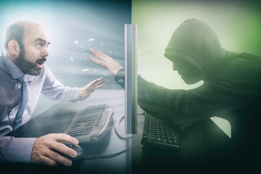 Left half of the picture is blue with a businessman using a mouse and keyboard looking scared with the right green half having a man with darkened obscured face in a hooded longsleeve shirt looking like a hacker putting his hand through the screen which is at the halfway point smashing it and glass flying towards the man