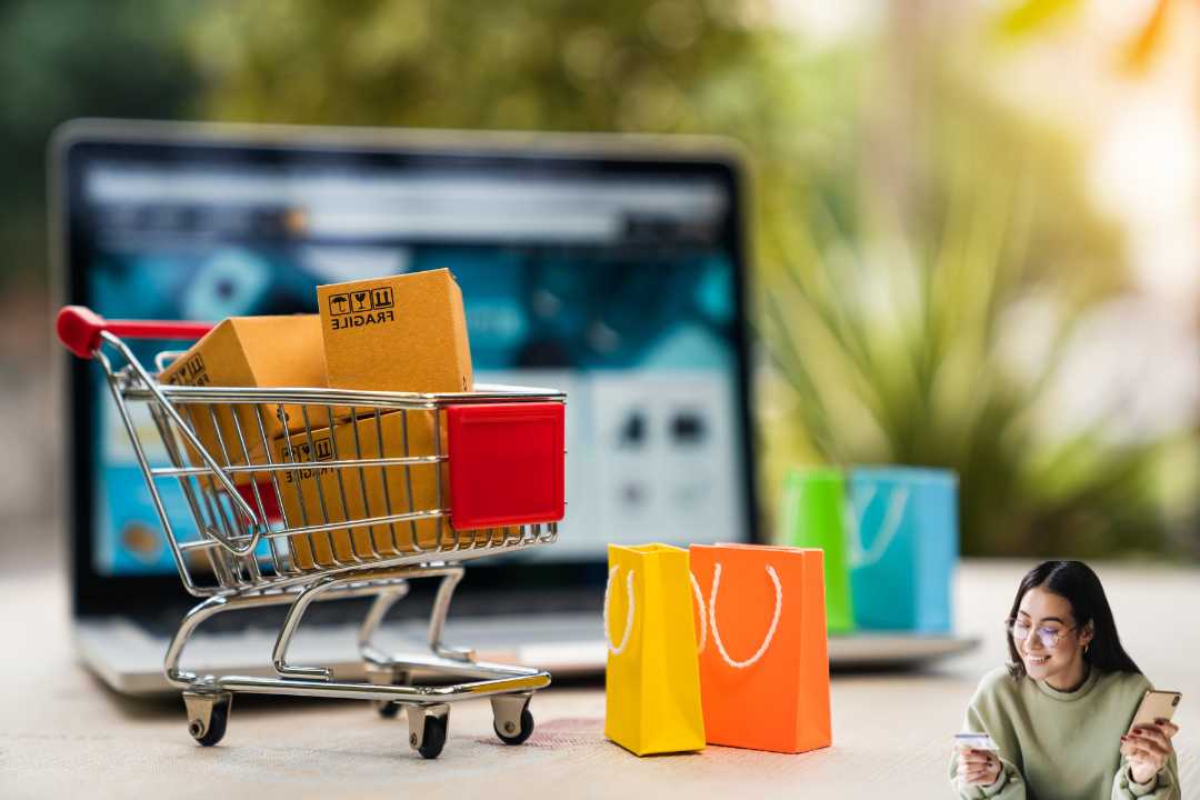 An optimised ecommerce store on a laptop screen in the background with a small shopping cart filled with boxes and colorful bags siting in front of the laptop, symbolising ecommerce. In the lower right corner, a person is holding a phone, possibly contemplating website optimisation strategies for their store.