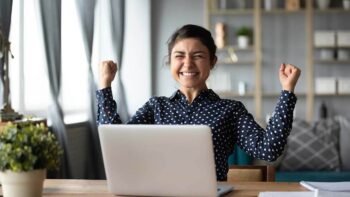 White Label Website Design embodied by a lady sitting at a desk with her laptop with a happy excited look on her face and arms bent up from elbows with fingers closed into fists in a yes type exclamation